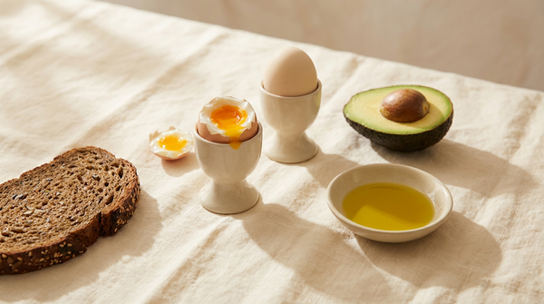 A breakfast of soft-boiled eggs, avocado, olive oil and seeded bread in bright morning light